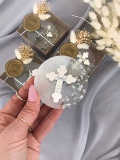 a person holding a small glass object with white flowers in front of two other items