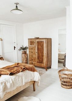 a bed room with a neatly made bed next to a wooden dresser and basket on the floor