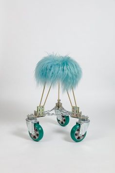 an artistic sculpture made out of metal and glass wheels with feathers on each wheel, sitting on a white surface