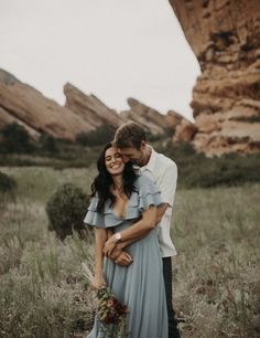 a man and woman standing next to each other in a field with mountains behind them