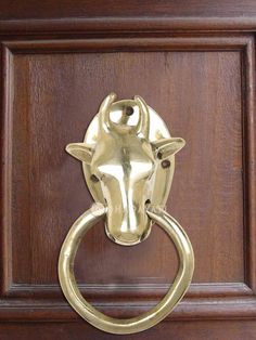 a brass cow head door knocker on a wooden door with an oval ring handle