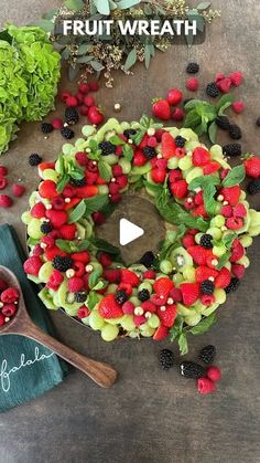 a fruit wreath with berries, raspberries and blackberries on the side next to a wooden spoon