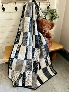 a teddy bear sitting on a bench next to a black and white quilt