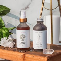 two bottles of liquid sitting on top of a wooden table next to a potted plant