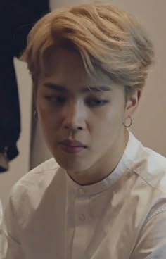 the young man is looking at his cellphone while wearing earrings and a white shirt