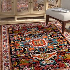 a blue rug with red, orange and yellow designs on it in front of a white chair