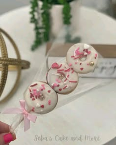 a person is holding two donuts with pink sprinkles on them and tied to a string