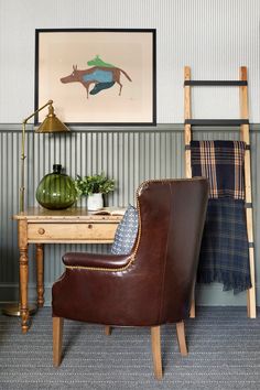 a chair sitting next to a table with a lamp on it and a painting above it