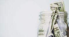 a jar filled with money sitting on top of a table next to a white wall