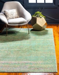 a green rug with a chair and plant in front of it on a wooden floor