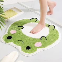 a person's feet on a green and white bathroom rug with pink flowers in the center