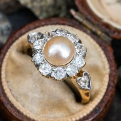 This elegant platinum topped, yellow gold ring is centered with a natural, post set pearl surrounded by ten (10) bead set, round old European cut diamonds. The shoulders are each accented with a heart detail, bead set with a round old European cut diamond. The ring measures 12.1mm at the top, rises 8.1mm above the finger, tapering to 1.2mm wide and 0.7mm thick at the base of the shank. This ring is currently a size 6.75. Pearl Diamond Ring, Pearl Necklace Vintage, Unusual Rings, Pearl And Diamond Ring, Diamond Halo Ring, Vintage Pearl, European Cut Diamonds, Halo Diamond Ring, Vintage Pearls