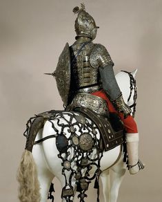 a man riding on the back of a white horse wearing a suit of armor and helmet