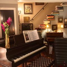 a black piano in a living room next to a stair case filled with books and flowers