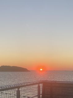 the sun is setting over the ocean with a fence in front of it and an island in the distance