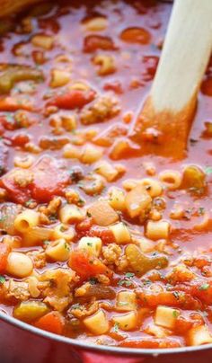 a red pot filled with pasta and meat in tomato sauce next to a wooden spoon