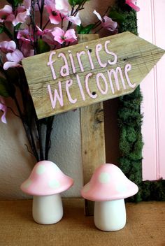 two pink mushrooms are sitting in front of a sign that says fairies welcome on it