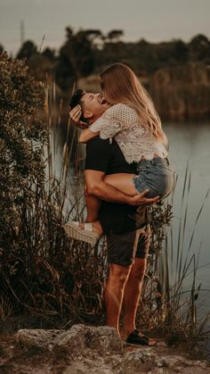 a man carrying a woman on his back by the water's edge while she is holding her