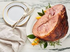 a ham is on a plate next to a fork, knife and napkin with flowers