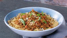 a blue bowl filled with pasta and meat on top of a gray table next to a brick wall