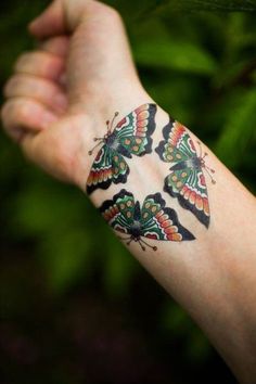 a butterfly tattoo on the arm of a person's left hand with green leaves in the background