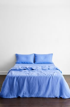 a bed with blue sheets and pillows in a white room next to a wooden floor