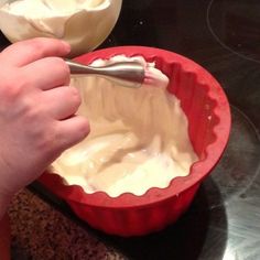 a hand holding a spoon in a red bowl filled with whipped cream on top of a stove