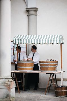 two men are standing under an umbrella selling food and drinks in buckets on the street