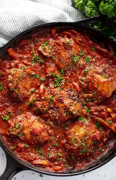 a skillet filled with meat covered in sauce and garnished with parsley