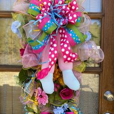 a pink and green wreath with polka dots, flowers, and a teddy bear hanging from the front door