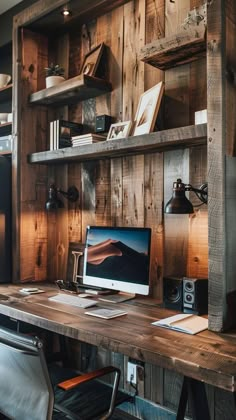 a wooden desk topped with a computer monitor next to a shelf filled with books and other items