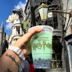 a hand holding up a cup with harry potter on it in front of a building