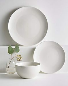 three white plates and two bowls on a table with a plant in the middle one is empty