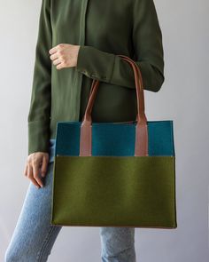 a woman is holding a green and blue tote bag with brown straps on it