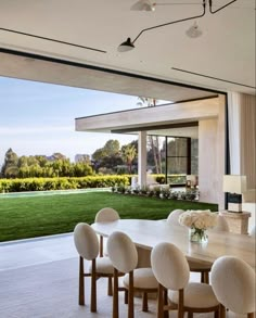 a dining room table with white chairs next to a large open window overlooking a lush green field