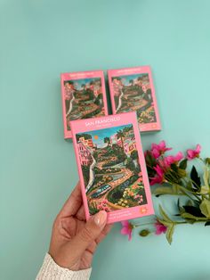 a person holding up three cards in front of a bouquet of pink flowers on a blue background