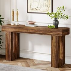 a wooden table with two vases on it in front of a painting and potted plant