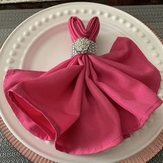 a pink napkin on top of a white plate with a diamond brooch in the center