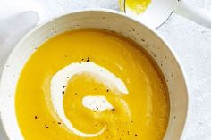 a white bowl filled with yellow soup next to a spoon and napkin on top of a table