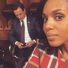 a woman sitting next to a man in a suit and tie on a cell phone