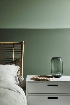 a bedroom with green walls and a white dresser next to a bed in the foreground