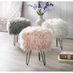 three sheepskin stools sitting on top of a wooden floor next to a vase with flowers