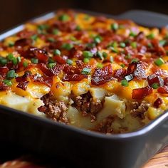 a casserole dish with cheese, bacon and green onions in it on a wooden table