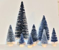 small christmas trees are lined up in rows on a table with candles and snow around them