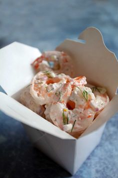 shrimp salad in a white paper container on a blue tablecloth with some garnish