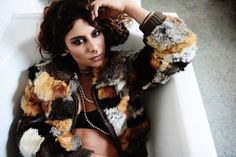 a woman sitting in a bathtub with her hands on her head and wearing a fur coat