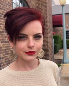 a woman with red hair and earrings standing in front of a brick building wearing a sweater