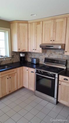 an empty kitchen with stainless steel appliances and wood cabinetry, including tile flooring