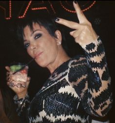 a woman is holding up her peace sign and drinking from a drink in front of a neon sign