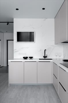 a kitchen with white cabinets and marble counter tops, along with an entertainment center on the wall